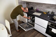 © Viktoriya - A man opens the dishwasher to unload clean dishes. A kitchen interior with white cabinets and wood floors