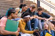 © Koldo_Studio - Group of happy young college friends sitting on university steps, sharing a moment, and enjoying a smartphone outdoors