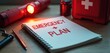 © Maryna - Emergency plan notebook, red flashlight, first-aid kit, and pen on desk. Preparedness for disaster response, safety, and survival essentials for crisis situations.
