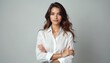 © Maryna - Pro woman stands with arms crossed. Young female wears white shirt, looks confident. Studio portrait with grey background. Brunette model has long hair. She appears stylish and elegant.
