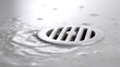 © twc - Close-up of a silver drain with clear water flowing and splashing around, creating small ripples and bubbles on a light surface, clean and fresh