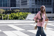 © wavebreak3 - African American teen woman walking across tiled plaza with phone and pink beanie, copy space