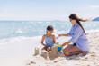 © anatoliycherkas - Mother and daugther building sandcastles at the beach, spending quality time together on summer vacation