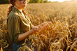 © maxbelchenko - A young farmer examines golden wheat ears in a field. A female agronomist inspects the quality of the crop at sunset. Concept of farming, agriculture. A bountiful harvest.
