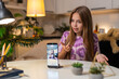 © Andrii Iemelianenko - Teenager girl at night home records social video on smartphone dances shows funny gesture joy. Caucasian child kid sitting at table at evening smiles waves hand starts vlog uses camera app posts clip.