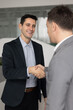 © fizkes - Smiling young adult Latin businessman exchanging handshake with male business partner in office satisfied with making successful mutual agreement based on partnership trust cooperation. Vertical image