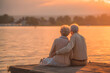© krasyuk - Elderly couple sits by the lake during sunset, enjoying their time together on a wooden dock surrounded by nature