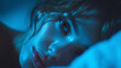 © CinimaticWorks - female person lying awake in bed at night looking at window with moonlight casting blue light highlighting trouble sleeping and insomnia issue