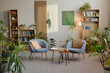 © Seventyfour - Modern psychology office interior featuring two empty armchairs facing small table with books, glass water carafe, clipboard and pen, surrounded by numerous green houseplants and bookshelves