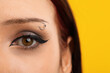 © New Africa - Woman with eyebrow piercing and perfect makeup on yellow background, closeup