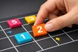 © Thitiporn - Strategic Planning: A hand meticulously places a colorful number block onto a grid, symbolizing the meticulous process of planning, strategy, and problem-solving.