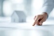 © KASUEMA SALAE - Close up of a professional hand pointing at a 3D architectural house model on a white desk, sharp focus, property planning