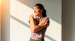 © Irina Kado - Woman crossing arms for shoulder stretch Female performing upper body flexibility exercise indoors in sunlight. Used for fitness training guides, physiotherapy content and healthy lifestyle promotion.