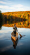 © PhotoArtHub - Image of a woman standing in a canoe on a lake during autumn, holding a paddle, reflecting colorful foliage. Represents adventure and tranquility