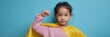 © Andrii Zastrozhnov - Confident asian female child looking at camera wearing yellow cape and pink sweater fist raised confident expression and proud stance on blue backdrop