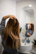 © Zoran Jesic - Woman styling long hair in bathroom mirror reflection