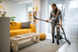 © Zoran Jesic - Woman vacuuming living room rug, cleaning home interior