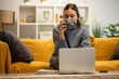 © Zoran Jesic - Woman drinking coffee using laptop on sofa at home