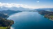 © Tyas - Aerial view captures vast blue lake nestled among rolling hills and distant snowcapped mountains under a bright sky