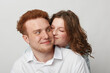 © SHOTPRIME STUDIO - Young couple with red hair and curly hair share a tender moment, woman hugging man from behind. Intimate love, affection, and happiness in a bright studio setting.