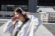 © wavebreak3 - Woman adjusting over-ear headphones while standing on urban rooftop plaza wearing white sweatshirt