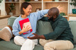 © djoronimo - Cheerful multiracial couple is having fun at home while while exchanging gifts.