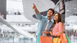 © Prostock-studio - A young couple is seen in a mall holding colorful shopping bags. The man points to something in the distance while the woman smiles. They look excited and happy during their shopping trip.