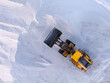 © AmazingAerialAgency - Aerial view of a yellow bulldozer amidst a sea of white salt mounds, a stark contrast under the clear sky, Aigues-Mortes, Occitanie, France.