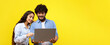 © Prostock-studio - Two people stand close together and look at a laptop screen. They are smiling and engaged with a bright yellow background. This scene shows a friendly moment of sharing and collaboration.