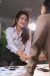 © Tj - Two smiling Asian businesswomen completing a professional transaction by shaking hands after a successful meeting, symbolizing agreement, collaboration, and trust in the workplace
