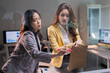 © Tj - Young Asian businesswomen collaborating, brainstorming, and writing ideas on a clear glass whiteboard in a modern office, developing a business strategy for future growth