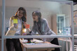 © Tj - Two Asian business women are brainstorming solutions and planning strategies in a modern office, working together on a clear glass board with colorful sticky notes and markers