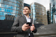 © muse studio - Businessman stands with phone and tablet outside modern office buildings in city center