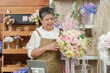 © Ekkasit A Siam - Elderly asian woman florist smiling while lifting colorful bouquet presenting product during video call with online customer in  flower shop showing personal floral selling experience after retirement