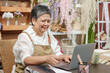 © Ekkasit A Siam - Asian senior florist woman looking at laptop screen with joyful face while checking successful online sales result at flower shop showing satisfaction from small business performance