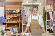 © Ekkasit A Siam - Mature asian florist standing proudly behind counter with laptop floral arrangements and business tools showing confidence in running successful online flower shop after retirement