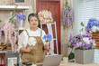 © Ekkasit A Siam - Mature Asian florist dancing joyfully holding artificial flowers while recording online class in cozy handmade flower shop decorated with floral displays laptop and teaching tools