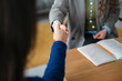 © Studio Marmellata - Two people shake hands over a desk with an open notebook and pencil, signifying agreement and partnership.