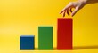 © Amal - Hand Reaching for Top of Red Bar Chart Blocks, Business Growth Concept, Bright Yellow Background, Studio Photography Mockup
