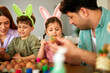 © djile - Family painting easter eggs together at table