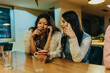 © qunica.com - Two women sit at a wooden table, talking on their phones. A casual, cozy cafe moment with coffee mugs and warm lighting.