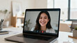 © phumin - Young woman smiling and looking at the camera during a video call on her laptop
