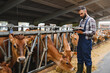© Serhii - Farmer using digital tablet while monitoring cows in barn