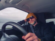 © mark_gusev - Male driver in his 40s or 50s in dark clothes and yellow hat and dark sun glasses. Man with grey beard behind driving wheel, happy friendly face Transport and tourism.