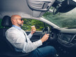 © mark_gusev - Bald man with grey beard is a car driver. Male in light blue shirt and dark glasses holding a brown cup with coffee, forest background. Transportation industry. Drinking energy drinks to stay awake.