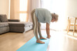 © Iuliia Versta/Stocksy - Senior Woman Practicing Forward Fold Stretch at Home