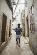 © Daniel Gonzalez/Stocksy - Young man walking and using smartphone in Stone Town alley
