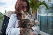 © Laura Herrera/Stocksy - Woman Holds a Cat While Sitting on a Balcony With Plants