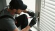 © junrong - A technician in work attire uses a screwdriver to repair a window lock mechanism indoors.