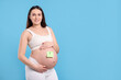 © New Africa - Choosing name for baby. Pregnant woman with note with question mark on her belly against light blue background, space for text